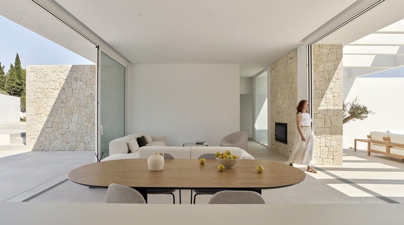 Open-plan living space with oval dining table and limestone clad columns framing courtyard views