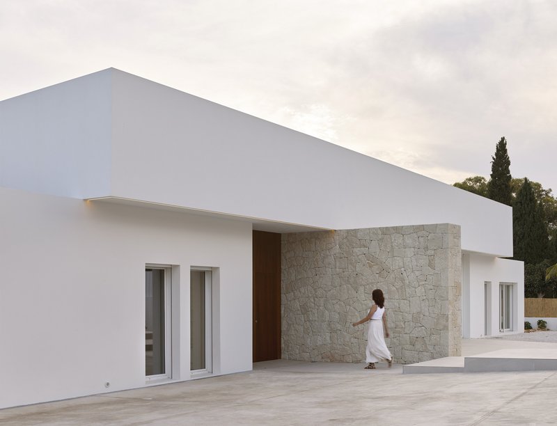 Recessed entrance with limestone wall panel and timber door as a figure approaches at dusk