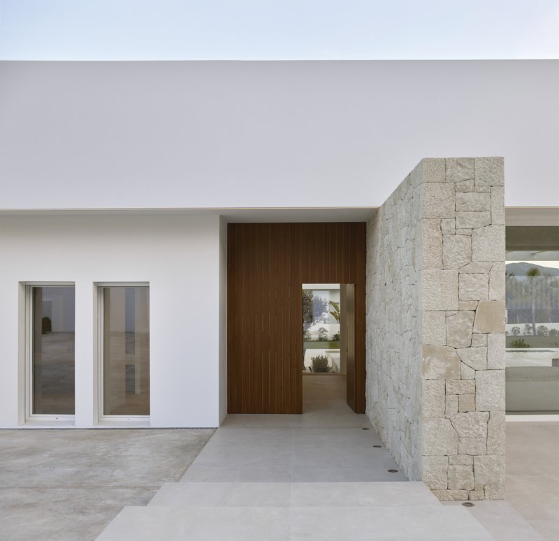 Covered entry with timber door and white stucco wall flanked by a limestone masonry column