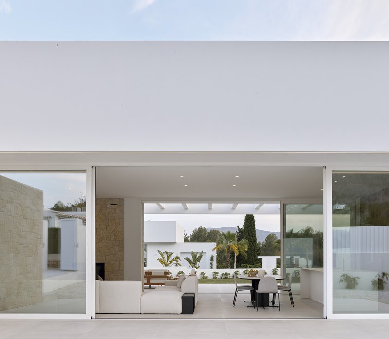 Open living pavilion with clerestory glazing framing courtyard plantings and cypress trees