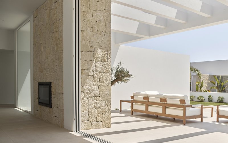 Interior threshold to poolside terrace with limestone fireplace wall and timber lounge chairs