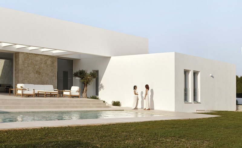 White rendered facade with two narrow windows and two figures standing beside a pool terrace