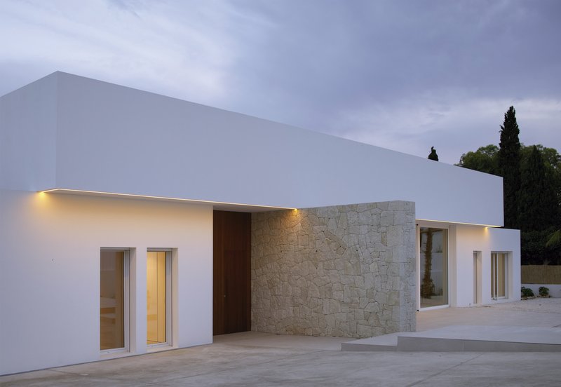 White stucco facade with stone accent wall and recessed lighting at dusk