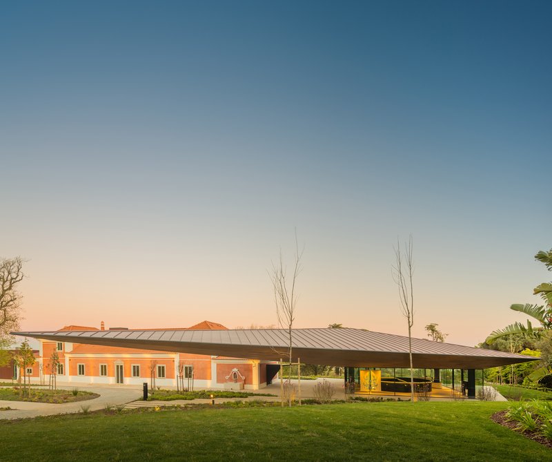 View of the red tile roof pavilion with metal canopy and young trees in the forecourt at dusk