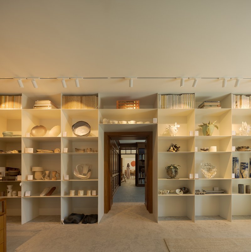 White shelving grid displaying ceramics and objects with a timber doorway framing a corridor beyond