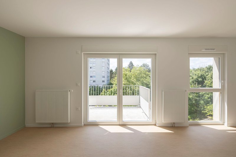 Bare interior room with pale wood flooring, wall-mounted radiators and sliding door to exterior balcony