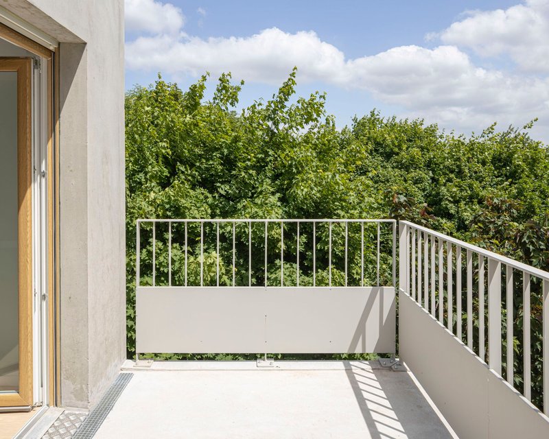 White balcony with metal railings overlooking dense green foliage under a partly cloudy sky