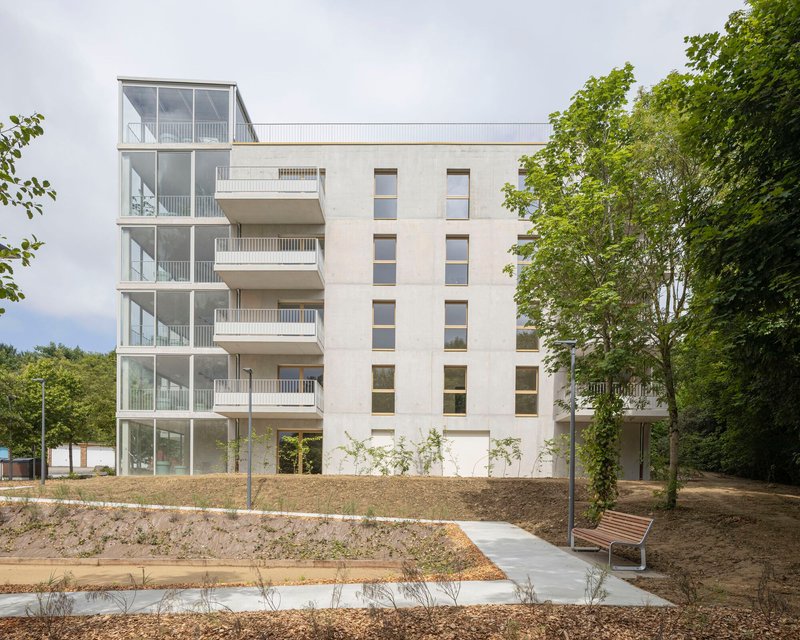 Multi-storey facade combining glazed balcony tower and rendered volume with punched windows beside newly planted landscape