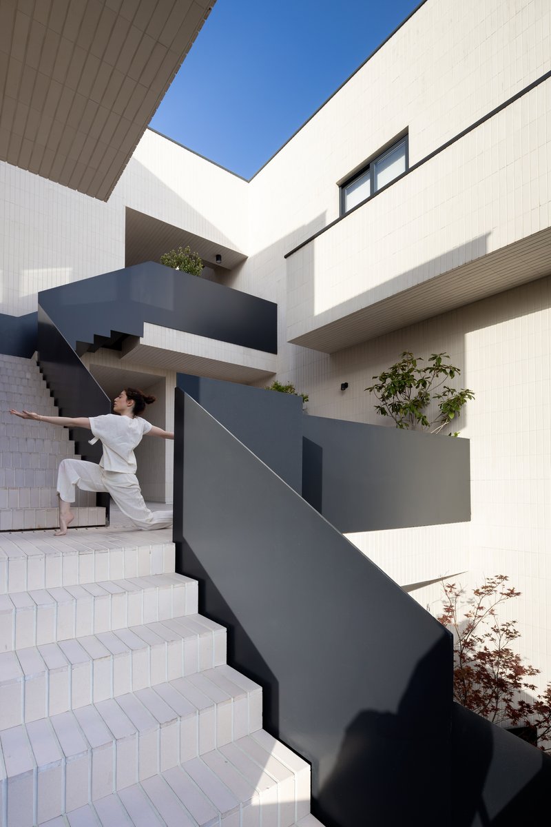 Exterior staircase with white tiled treads and black metal railings where a person stretches in sunlight