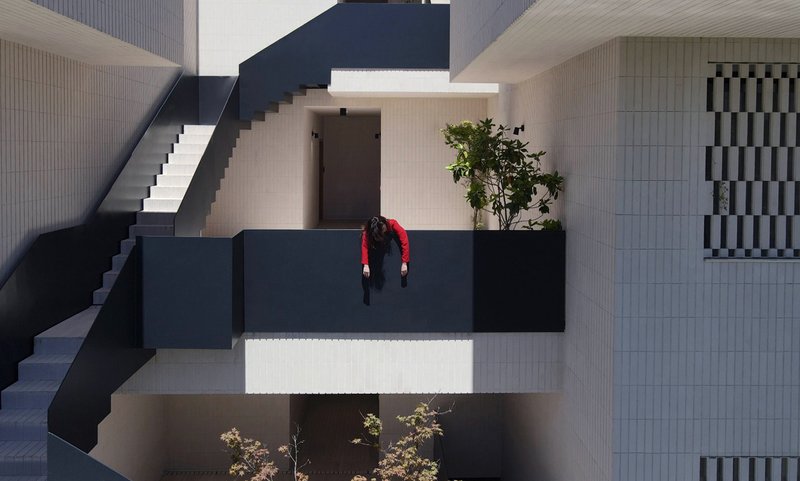 Overhead view of a figure in red leaning over the black steel railing of a courtyard bridge