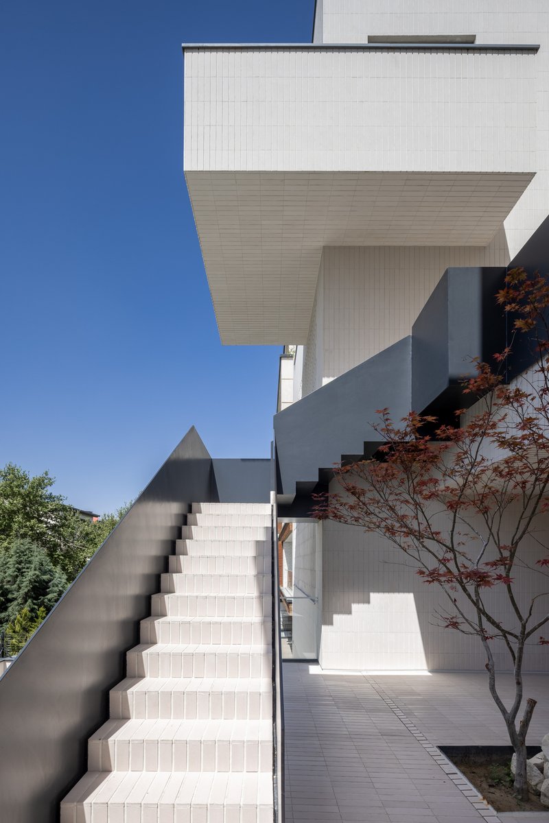 Exterior staircase with white tiled risers and dark metal handrail ascending between cantilevered volumes