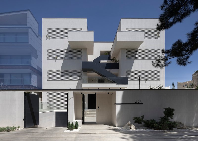 Street facade with white vertical louvers, cantilevered black balconies and an external staircase under clear skies