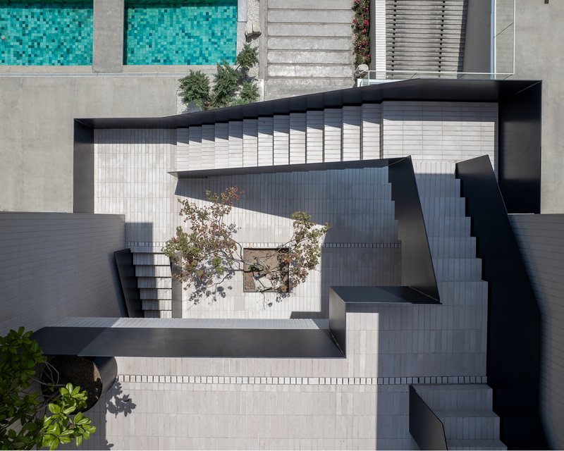 Top-down view of the zigzagging black staircase connecting multiple terrace levels with small planted trees below