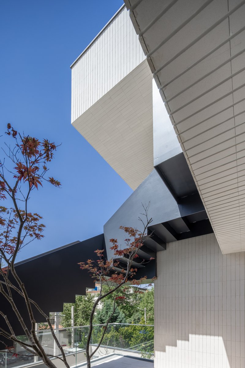 Stacked cantilevered volumes clad in white and dark metal panels beside a Japanese maple