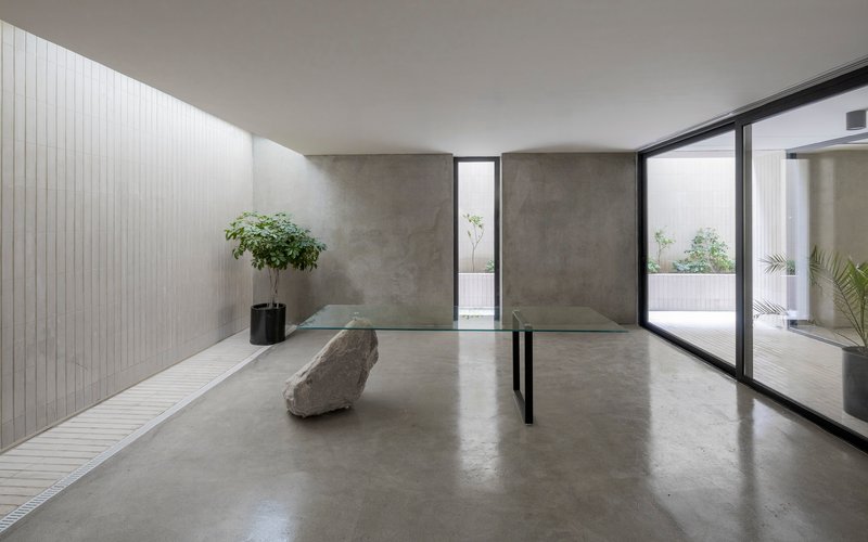 Polished concrete floor gallery with raw stone sculpture and glass doors opening to terrace