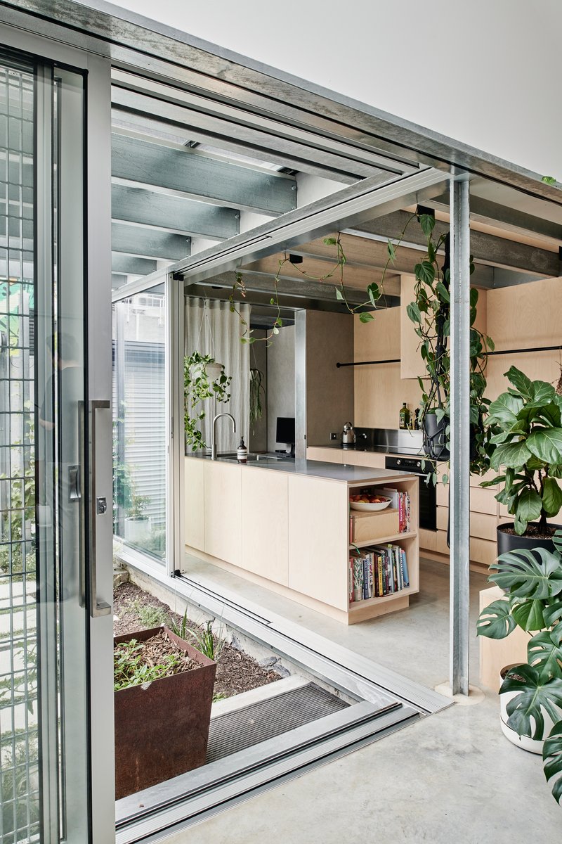 Open sliding glass doors revealing the kitchen and steel structural frame with hanging plants