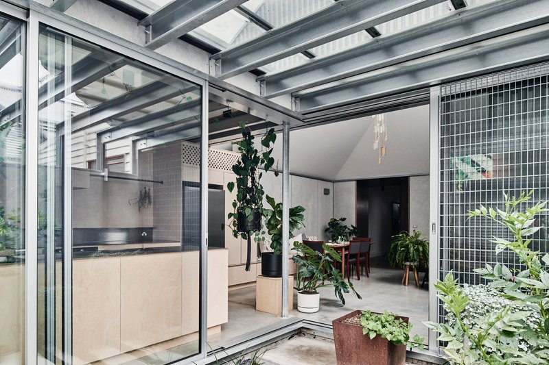 Interior looking through the glazed steel structure connecting kitchen and dining spaces with planted courtyard