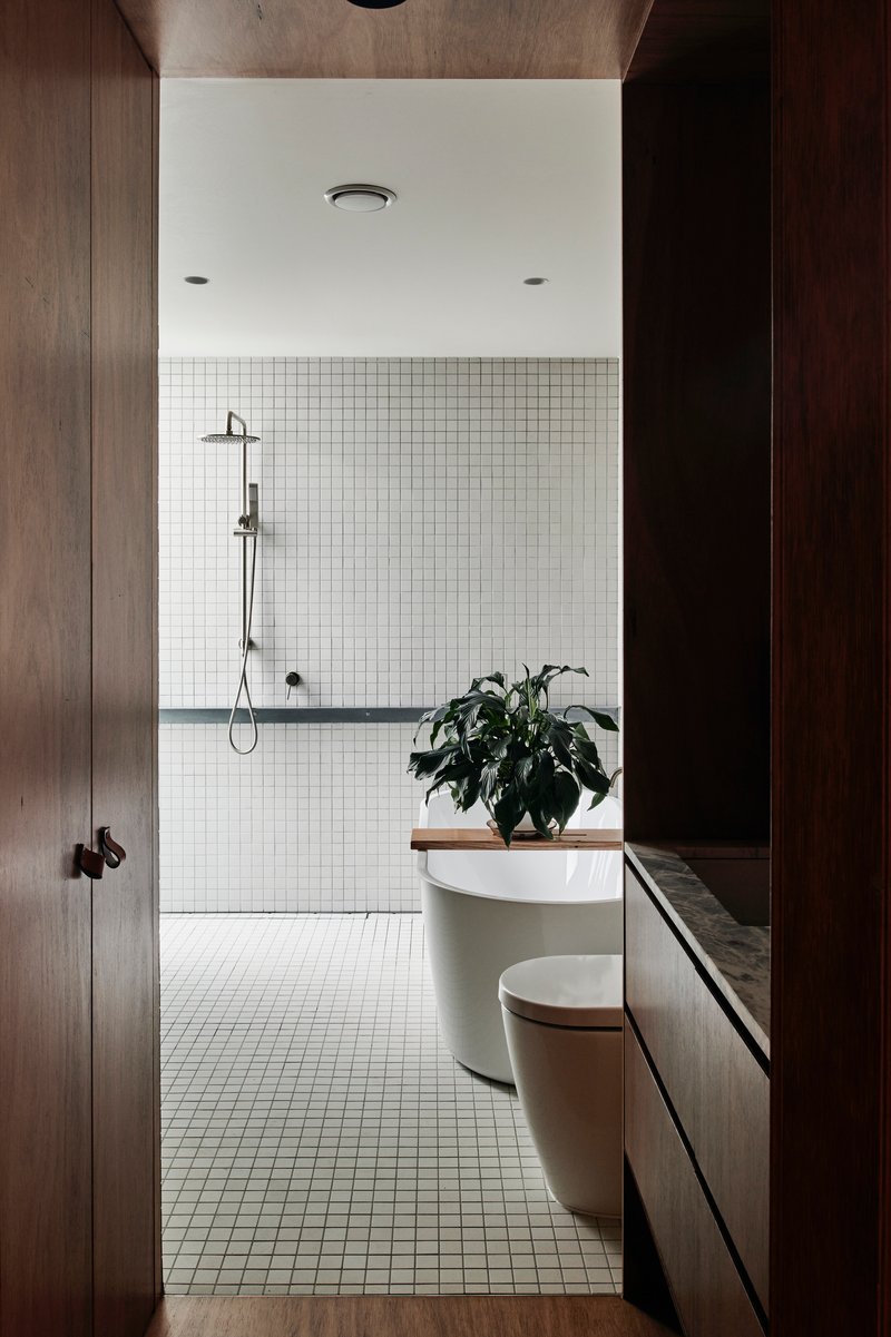 Bathroom with white mosaic tile walls, freestanding tub, and timber vanity under potted plant