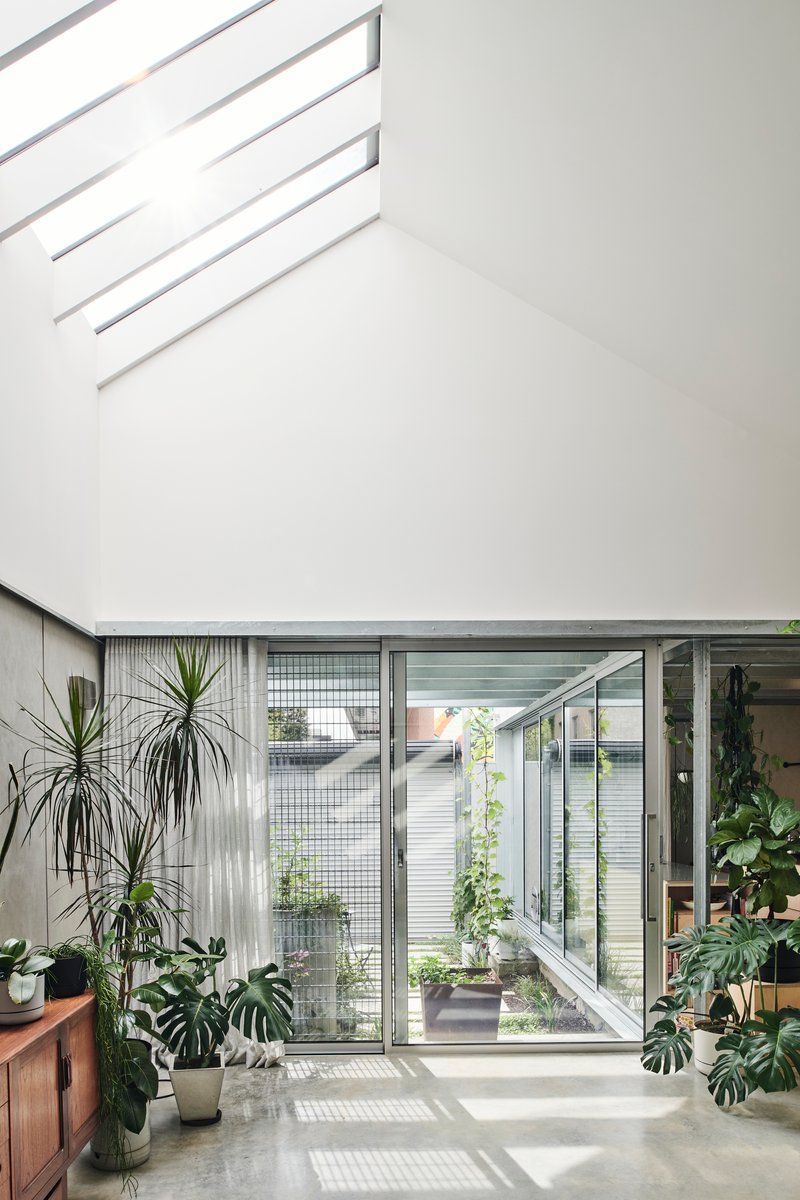 Double-height atrium space with glazed walls opening onto a tiled courtyard filled with potted plants