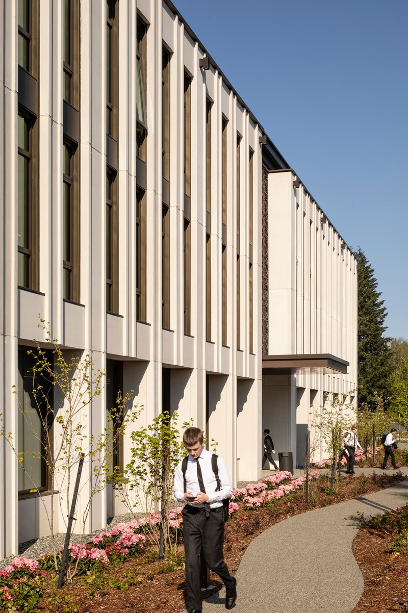 Side facade with vertical white fins and planted beds along the curving walkway in afternoon sunlight