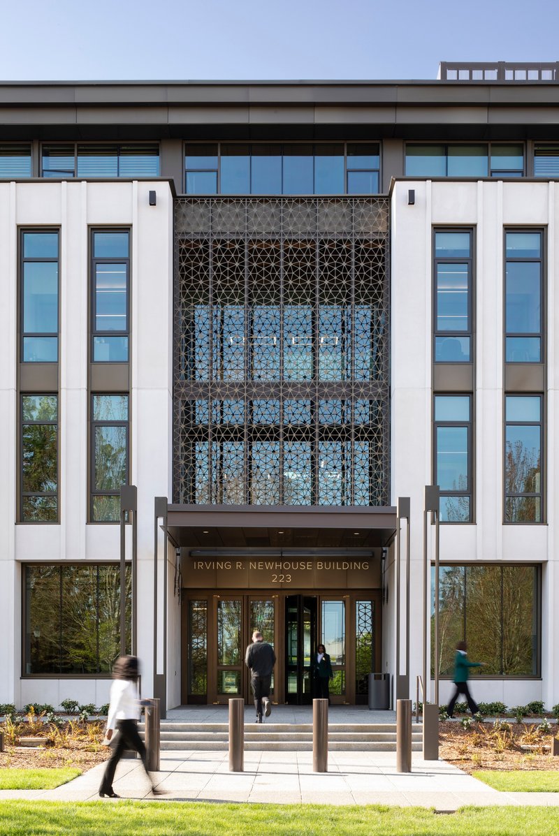 Main entrance facade with geometric patterned screen above glass doors and people walking on the pathway