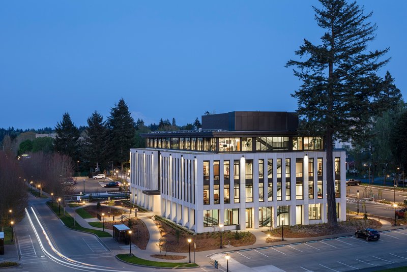 Aerial twilight view showing the corner entrance and dark rooftop volume above the illuminated glass base