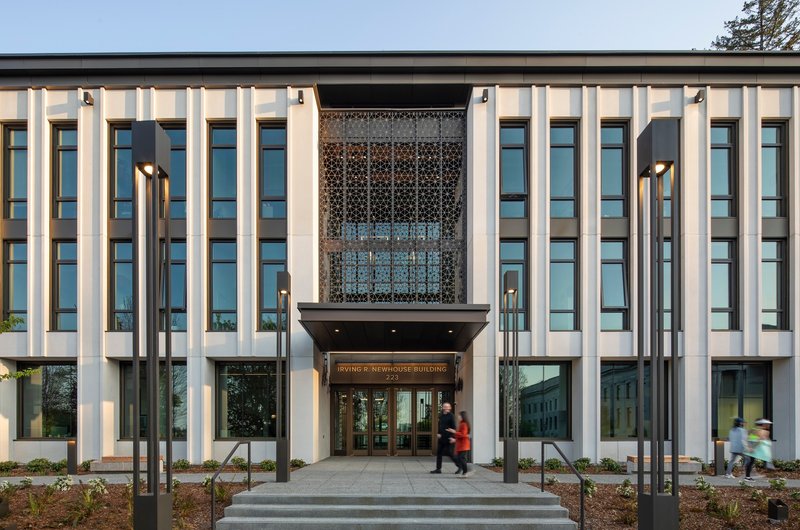 Entry facade showing vertical fins flanking a perforated metal screen above glazed doors with people entering at twilight