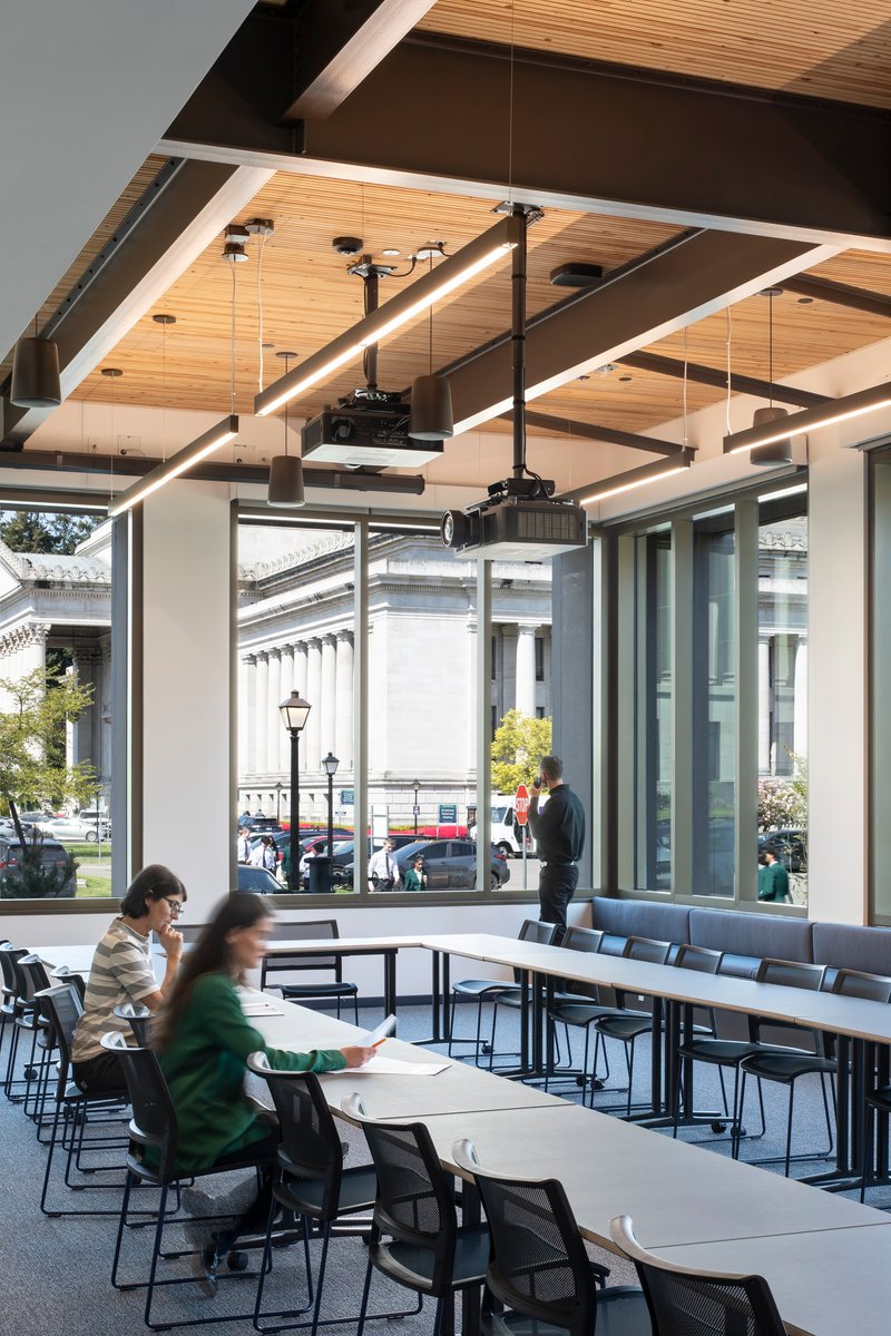 Dining area with timber-lined ceiling and floor-to-ceiling windows overlooking a street with pedestrians