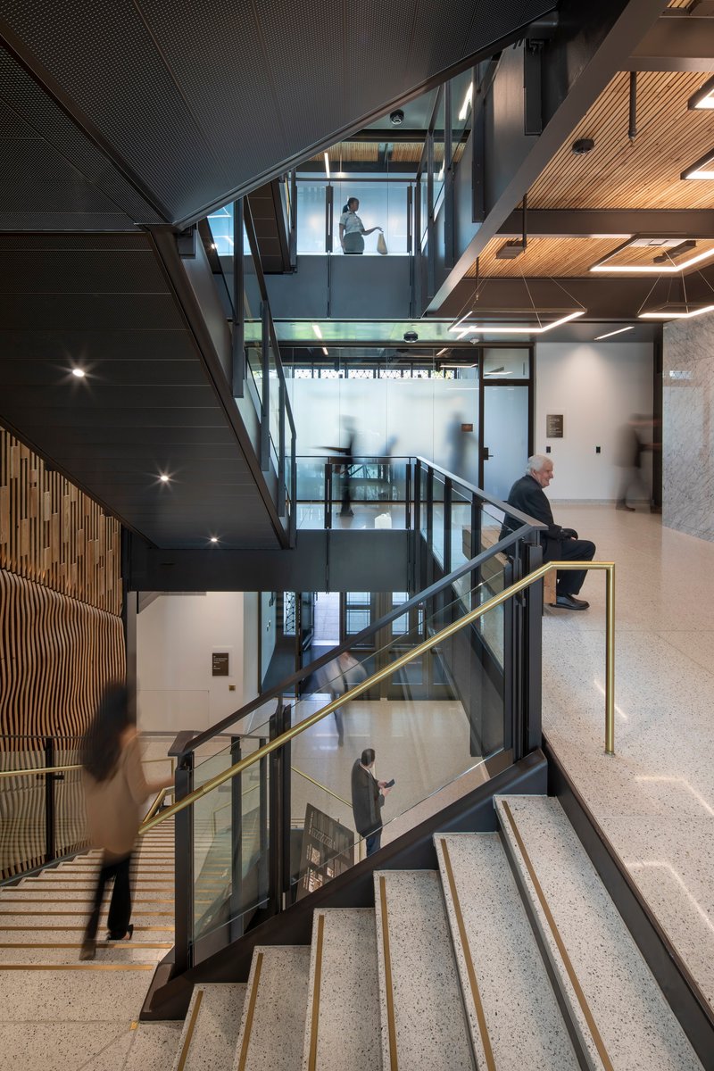 Multi-story atrium with interconnected steel staircases and glass balustrades under dark perforated ceiling panels