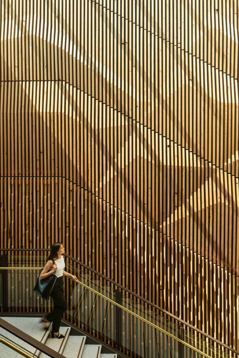 Person descending stairs alongside a patterned vertical timber screen with offset slats forming diagonal lines