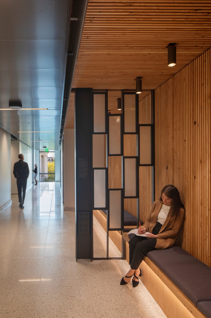 Corridor with slatted timber ceiling and geometric seating nook where a person reads