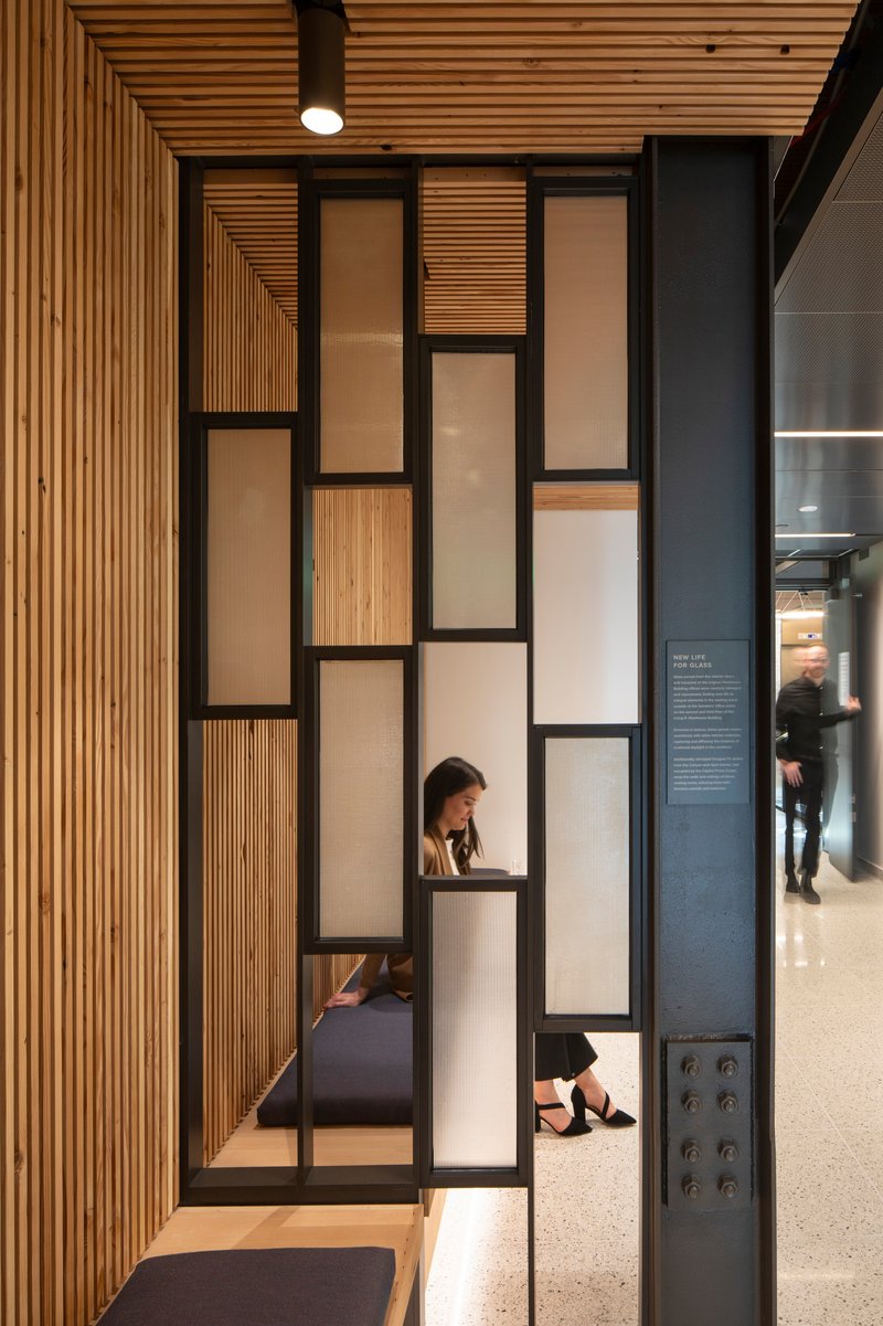 Black steel frame partition with alternating timber and frosted glass panels beside timber slat wall