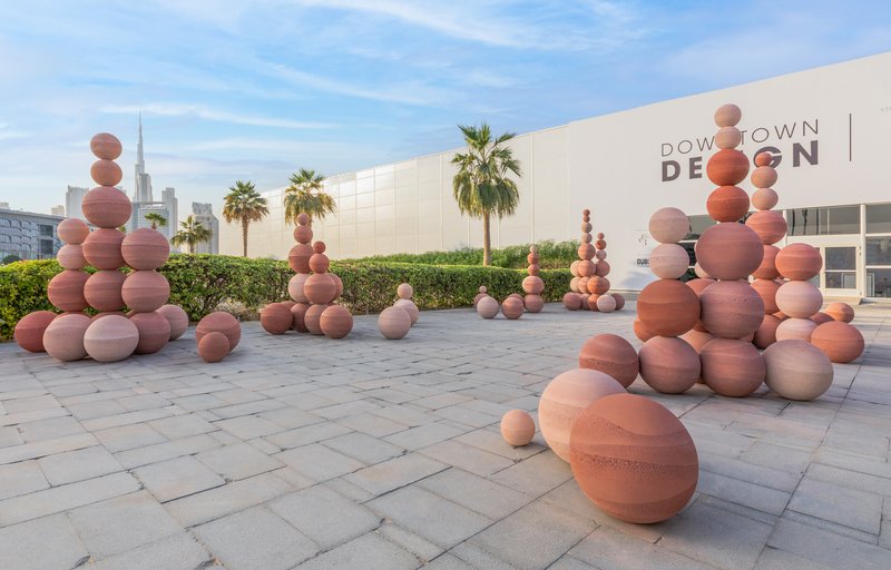 Terra-cotta sphere clusters scattered across paved forecourt with palm trees at dusk