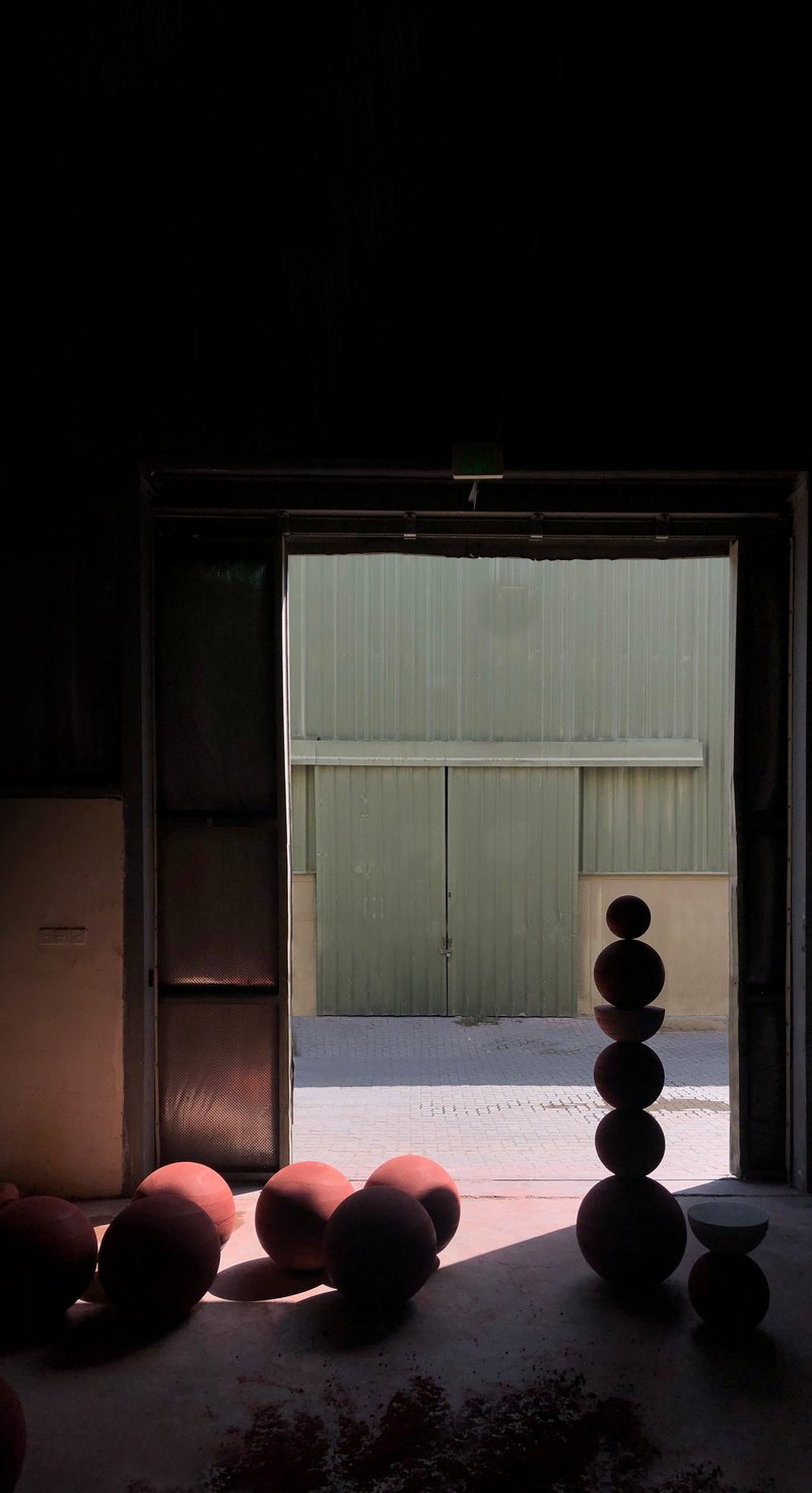Doorway framing stacked spherical sculptures in shadow with sunlit courtyard and green metal doors beyond