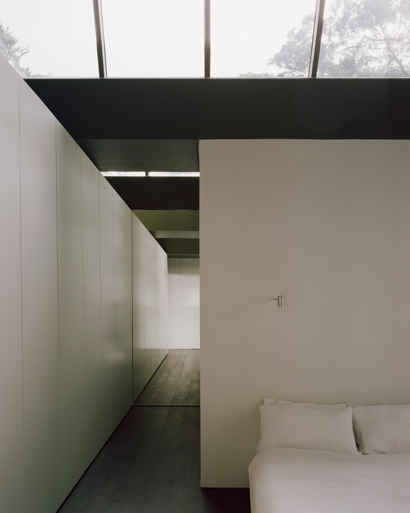 Bedroom with dark timber flooring and glimpse of adjoining spaces through tall steel-framed glazing