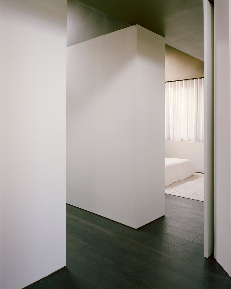 Freestanding plaster volume dividing circulation space from bedroom with vertical blinds