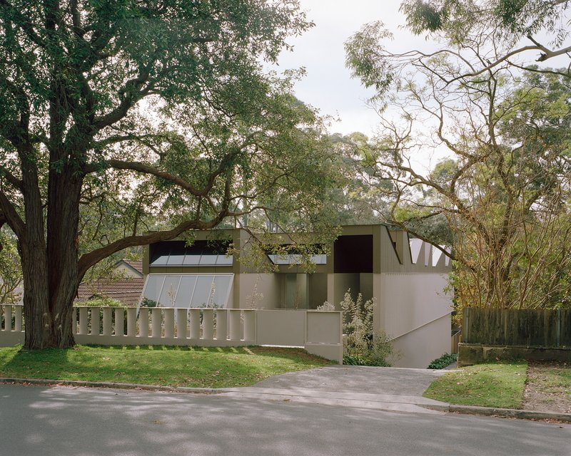 Street view of the muted green facade with clerestory windows beneath overhanging tree branches