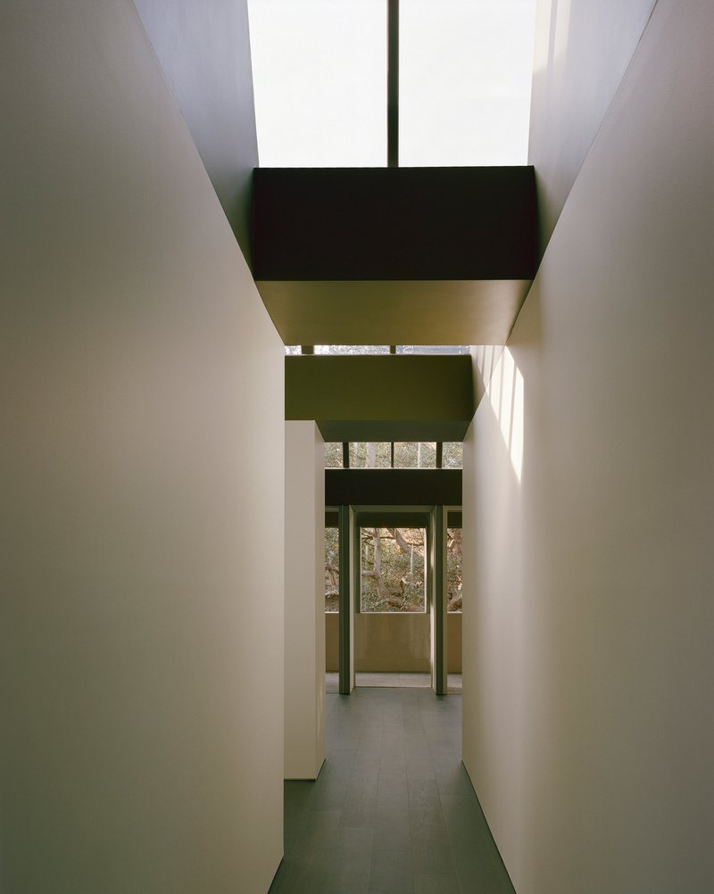 Narrow corridor with stacked clerestory volumes casting daylight onto pale plaster walls