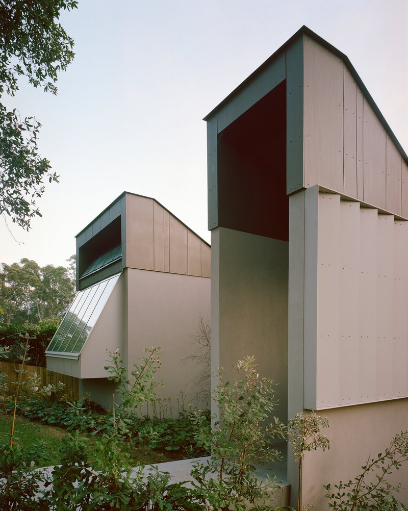 Angled view of the grey metal panel facade and gabled volumes rising above young planted trees
