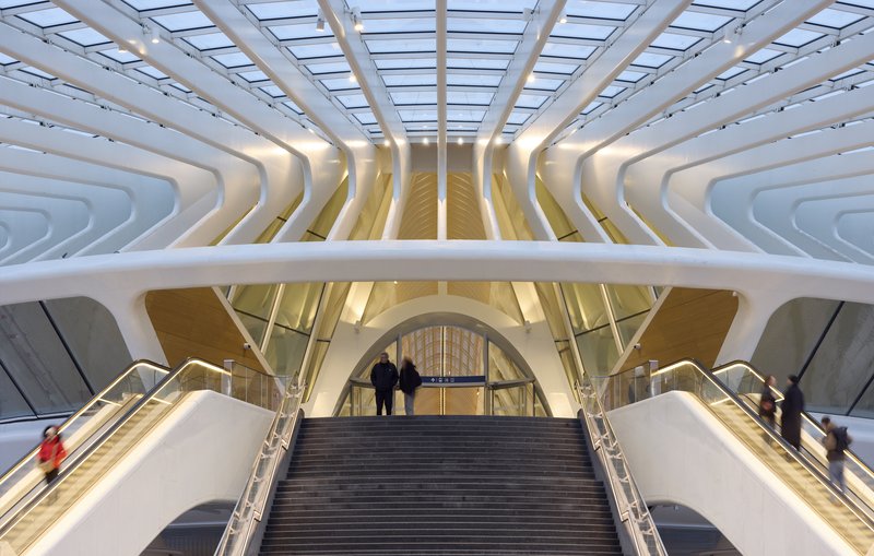 Escalator rising beneath the layered white ceiling ribs and glass skylight with passengers descending