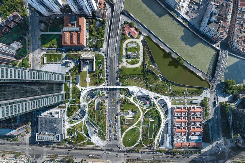 Drone view showing the looping pathways and green roofs adjacent to a river and roadway