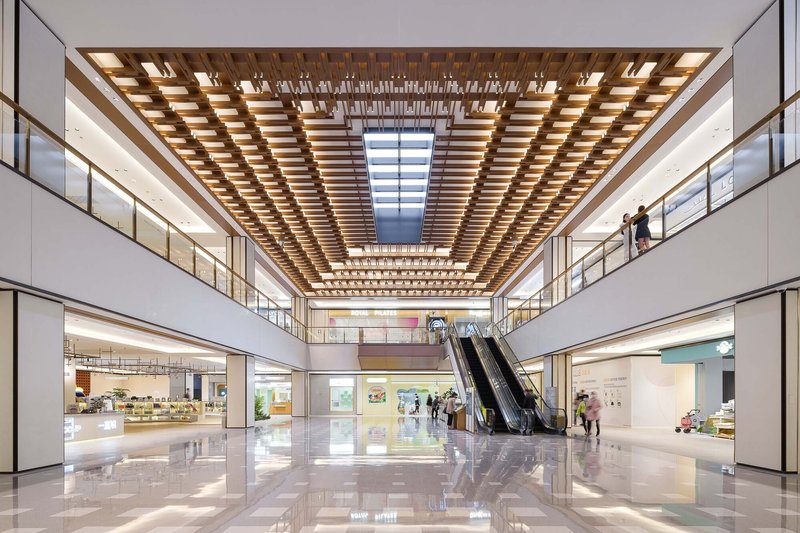 Interior atrium with gridded timber ceiling and escalators connecting multiple retail levels
