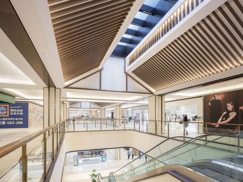 Multi-story void with angled timber slat ceiling planes intersecting beneath linear skylights