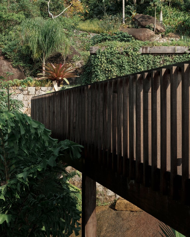 Curved timber balustrade with vertical slats cantilevered above planted hillside and stone retaining walls