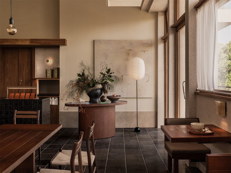 Dining space with timber ceiling beams, tall window, and paper lantern beside floral arrangement
