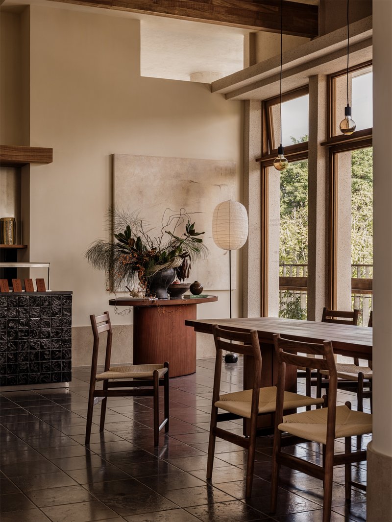 Double-height dining area with exposed timber beams and full-height glazing overlooking greenery