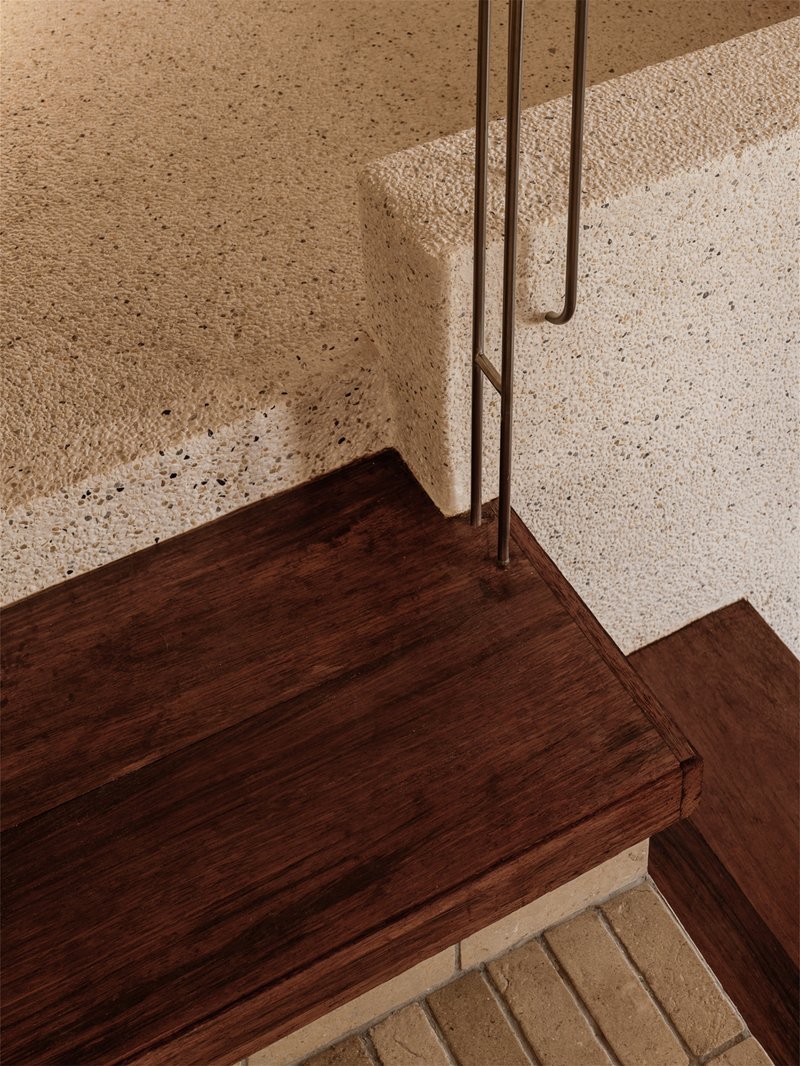Top-down view of dark timber stair treads cantilevered from a textured terrazzo wall with metal handrail