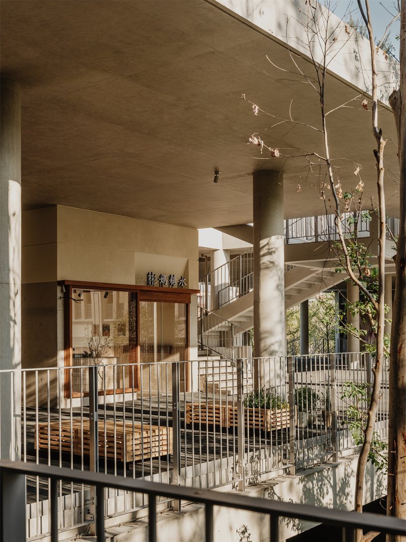 Interior courtyard with cylindrical columns, metal railings, planted balconies, and dappled sunlight through bare branches