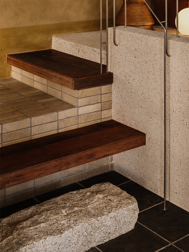 Stair detail showing timber treads supported by cream brick risers meeting a terrazzo wall with metal railing