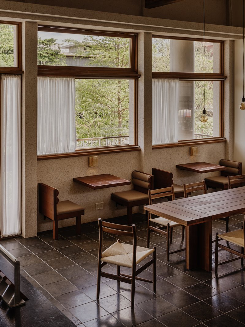 Dining area with timber-framed windows, built-in bench seating, pendant lights, and green foliage visible outside